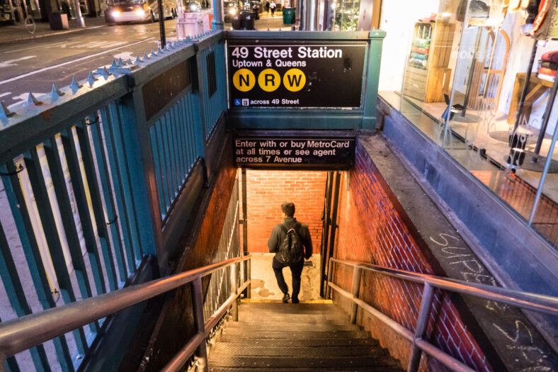 View down into lighted subway station in Manhattan at night with man on stairs