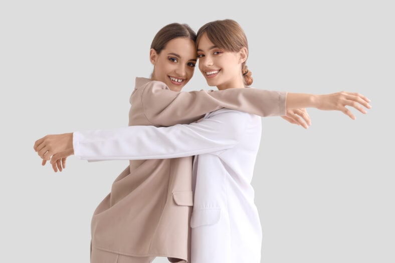 Beautiful young happy fashionable sisters in stylish outfits posing on grey background