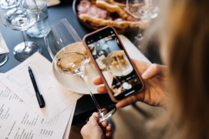 Woman photographing wine and charcuterie with smartphone