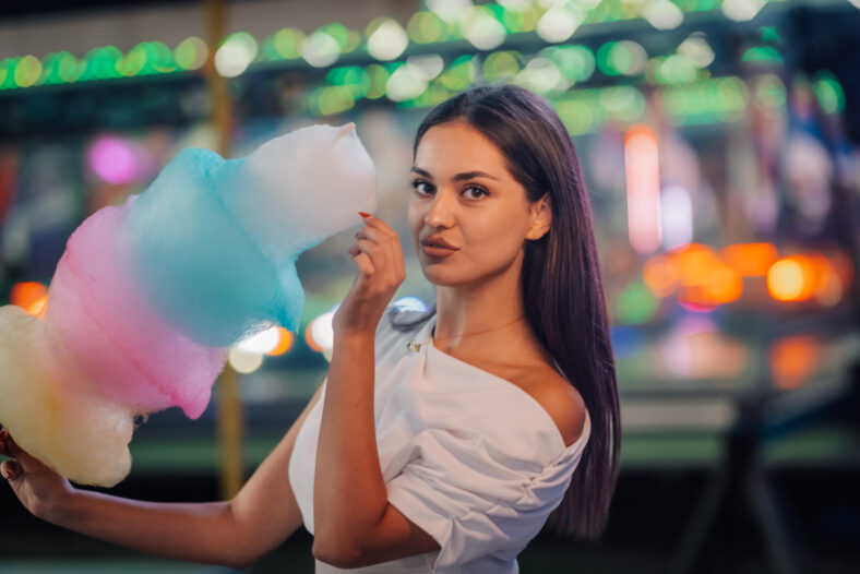 Young woman tasting a colorful cotton candy at the amusement park, enjoying the fun and festive atmosphere