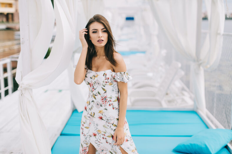 Portrait of a beautiful woman in a dress posing on a white wooden beach of summer.