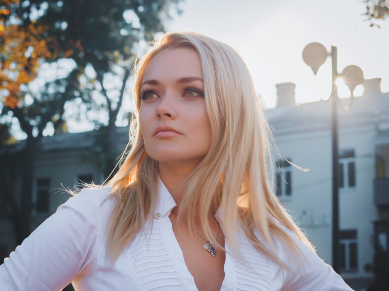 Portrait of young happy blonde business woman in the city. Beautiful girl in white sexy blouse in the street.