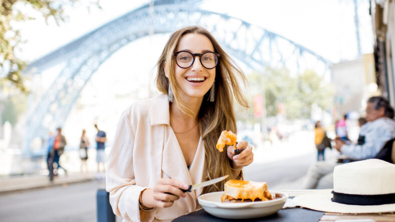 Woman eating traditional portuguese sandwich with meat called francesinha sitting at the restaurant in Porto city, Portugal