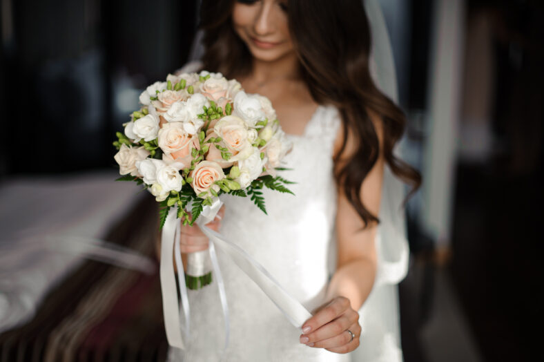 Bride morning preparation. Beautiful bride dressed in a white dress and veil holding a lovely wedding bouquet of flowers
