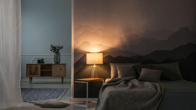 Bedroom interior at night with warm light of lamp on a bedside table near a wooden cupboard
