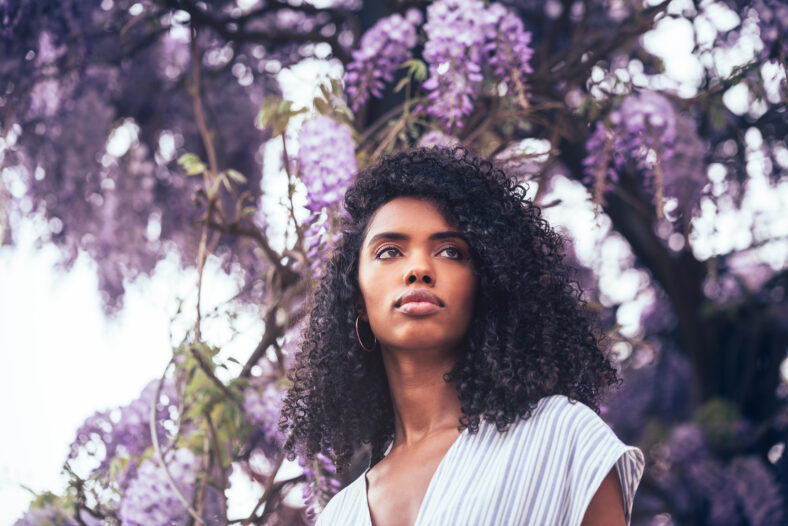 Thoughtful young black woman sitting surrounded by flowers