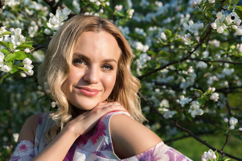 A girl with light wavy hair and in a bright dress near blossoming trees in the park