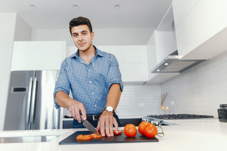 Man in a kitchen. A handsome man cut the tomatoes with a knife. Male at home with vagatables.