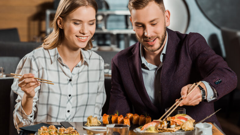 Attractive lovely couple eating together sushi rolls in restaurant