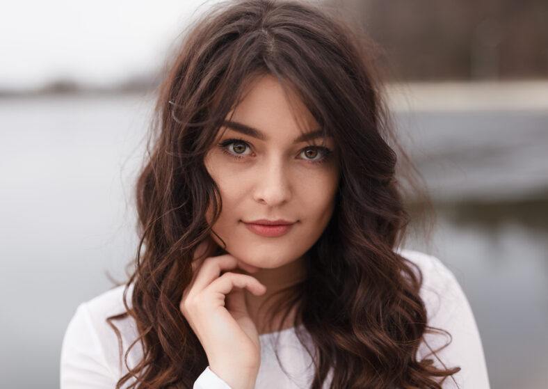 Portrait of gentle girl with brown wavy hair looking sensually at camera