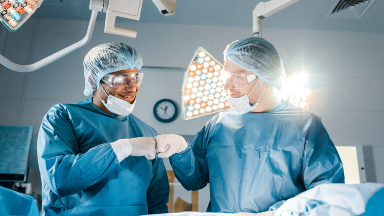nurse and surgeon in uniforms doing gesture and smiling in operating room