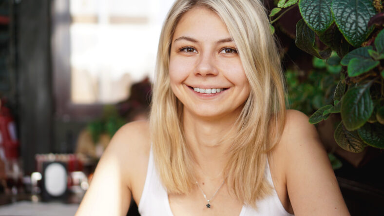Portrait of smiling blonde sitting at coffee shop near green plants