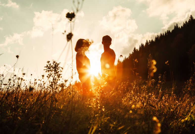 In love couple silhouets among high grass on sunset meadow