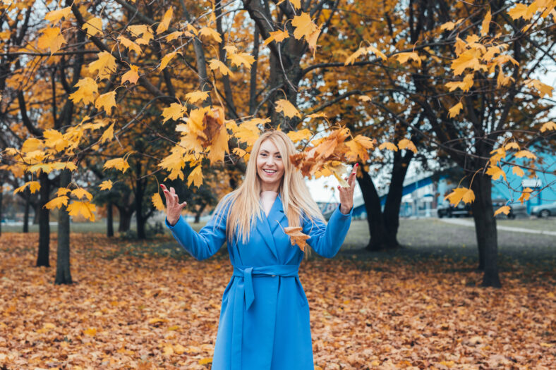 Portrait of a happy mature blonde woman playing with autumn leaves in park