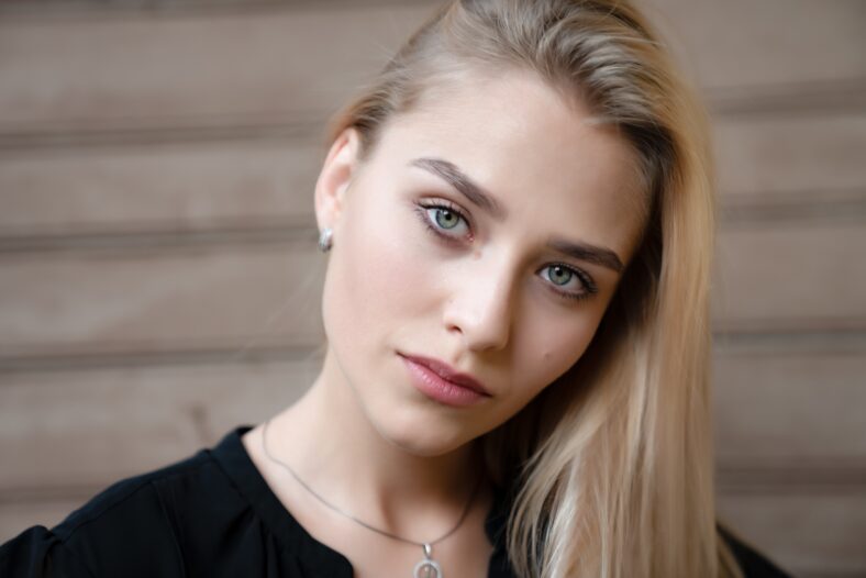 Close up portrait of a blonde young woman with healthy skin and blue eyes that looking at the camera, wooden background