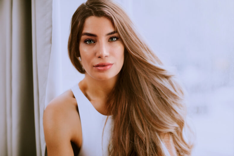 Pretty young long hair female brunette in front of the window