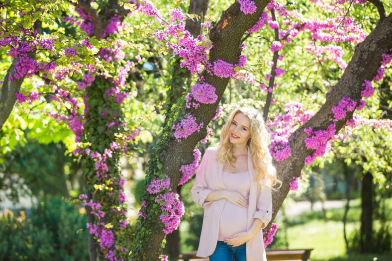 Young beautiful pregnant blonde. Stylish woman in the flowered park. Waiting for the baby