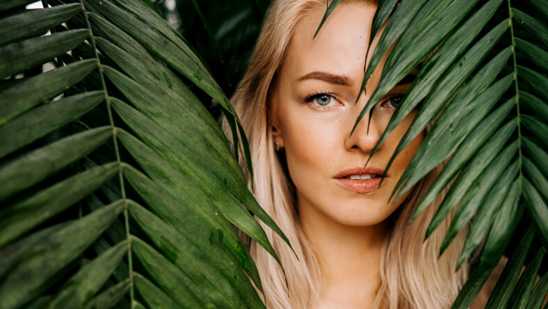 Young woman's face surrounded by tropical leaves.