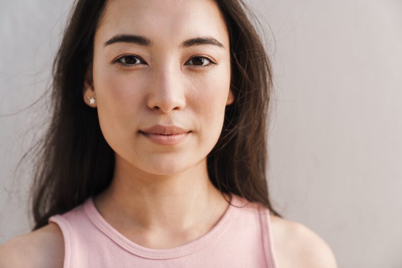 Image of young asian beautiful girl looking at camera while posing against white wall outdoors