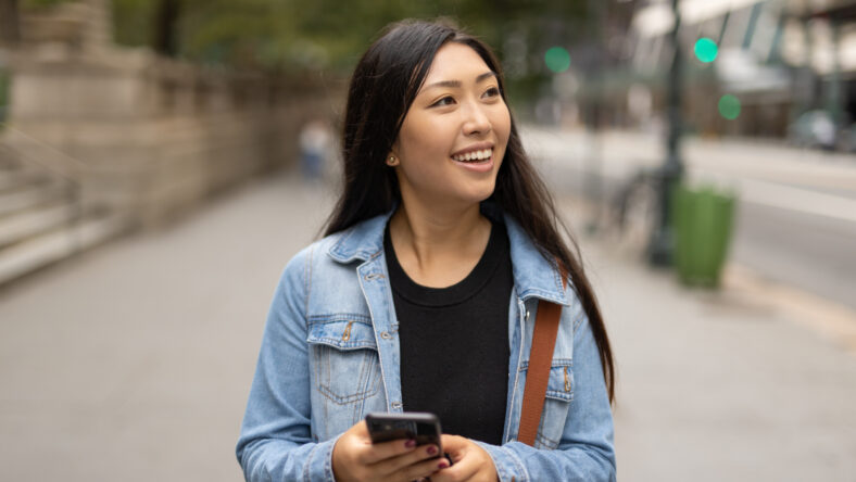 Young Asian woman walking street texting cellphone