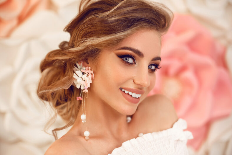 Beautiful young bride with makeup and fashion wedding hairstyle. Closeup portrait of young gorgeous woman over roses flowers. Studio shot.