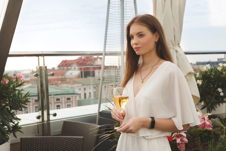 Gorgeous young woman waiting for someone on baer terrace, drinking wine