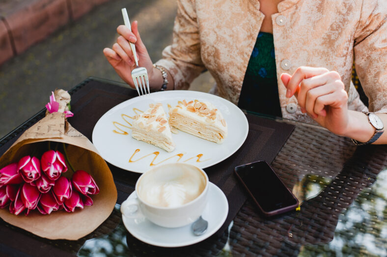 young stylish woman sitting in cafe, holding drinking cup cappuccino, eating tasty cake, tulips, happy birthday party, europe vacation, detail, close up hands, romantic dinner