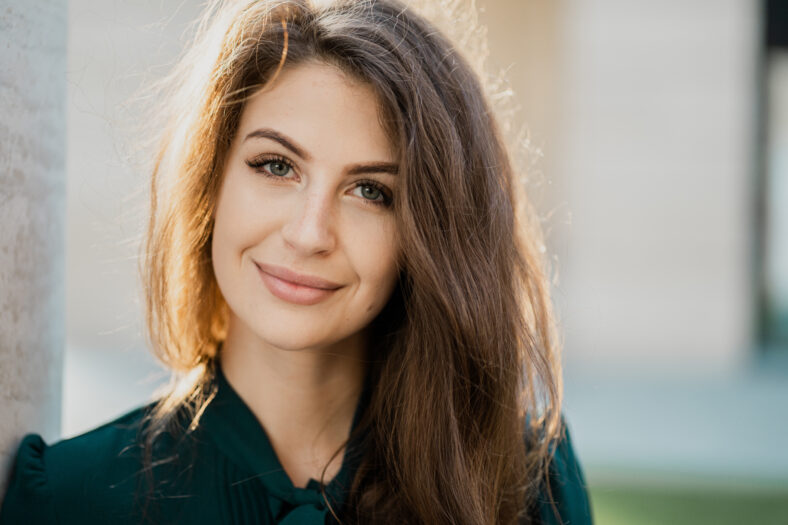 business woman confident smart teacher management student brunette of European appearance standing on the street smiling in a green dress and looking at the camera. Sunny day business center