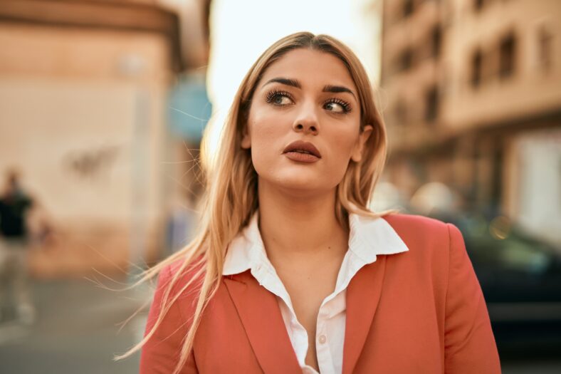 Young blonde businesswoman with serious expression standing at the city.