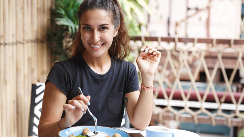 Eating out, lifestyle and travelling concept. Portrait of pretty european woman eating at restaurant table healthy food, drinking coffee, dining alone, smiling, tourist at cafe of her hotel.