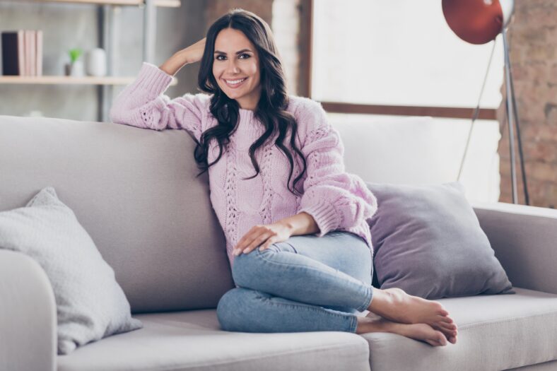 Full length photo of charming lovely attractive young woman sit sofa hold hand head good mood indoors inside apartment.