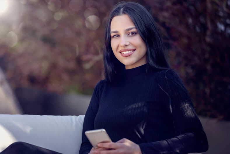 Portrait of a young woman with long black hair sitting outdoors in sunlight
