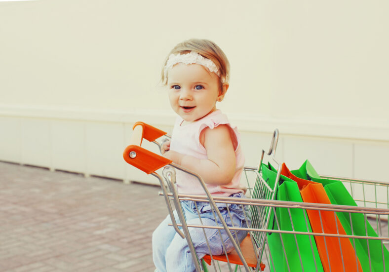 Happy baby with shopping bags sitting in a trolley cart in a city
