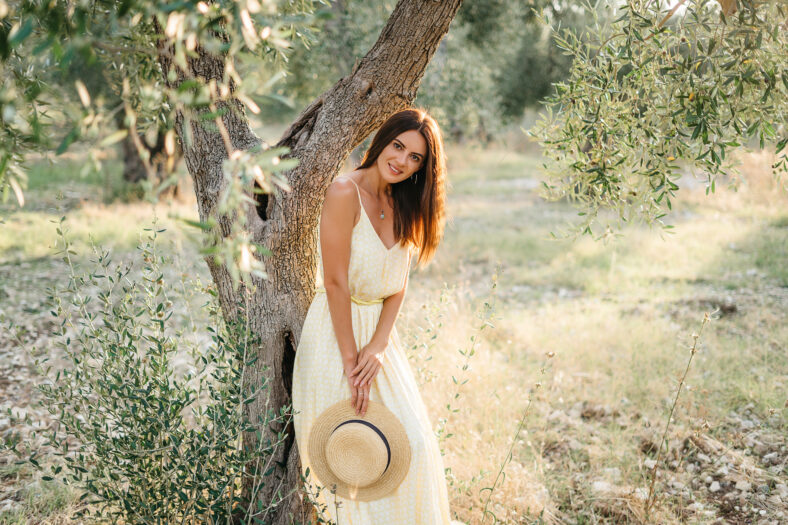Tender portrait of beautiful brunette woman in beautiful sunlight. Woman in yellow summer linen dress in olive tree garden. Natural beauty.Travel to Italy, summer vacation. High quality photo