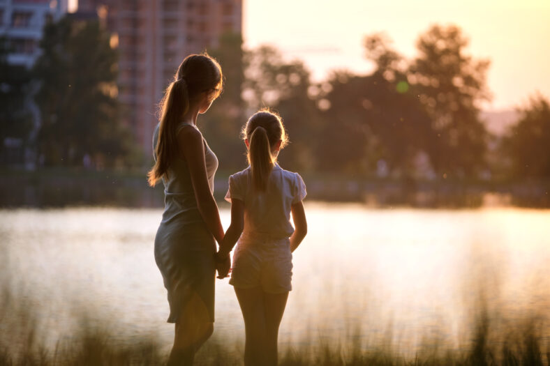 Happy mother and daughter standing together looking at building under construction dreaming about their future home at sunset. Family love and relationship concept.