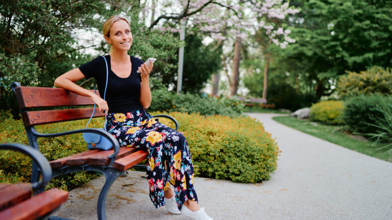 Attractive young woman using smartphone while sitting at the city park.