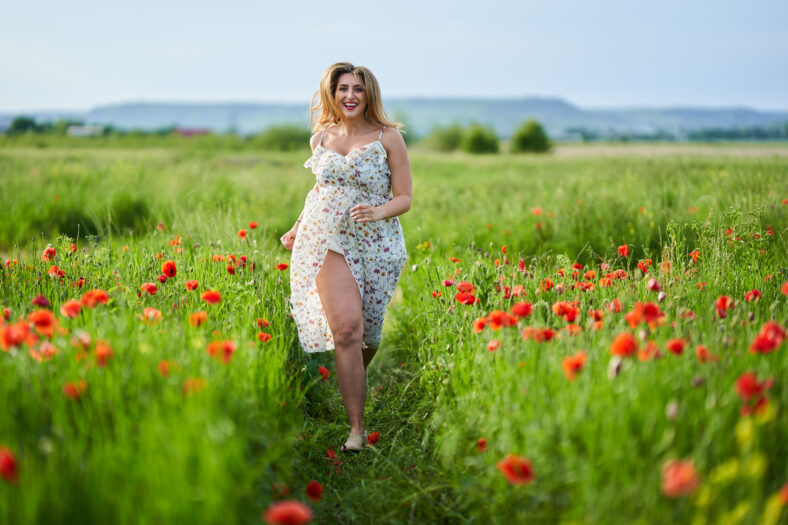 Beautiful plus size young woman in floral dress in a poppy field