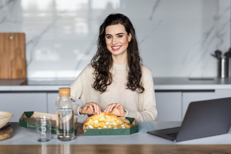 Overworked woman taking a break and eating pizza, working from home on laptop