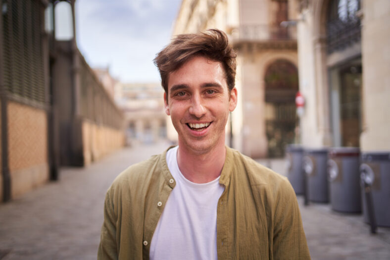 Close up portrait of happy young European man happy smiling face on street. Male people with cheerful expression looking at camera in open air. Nice boy posing for photo outdoor.