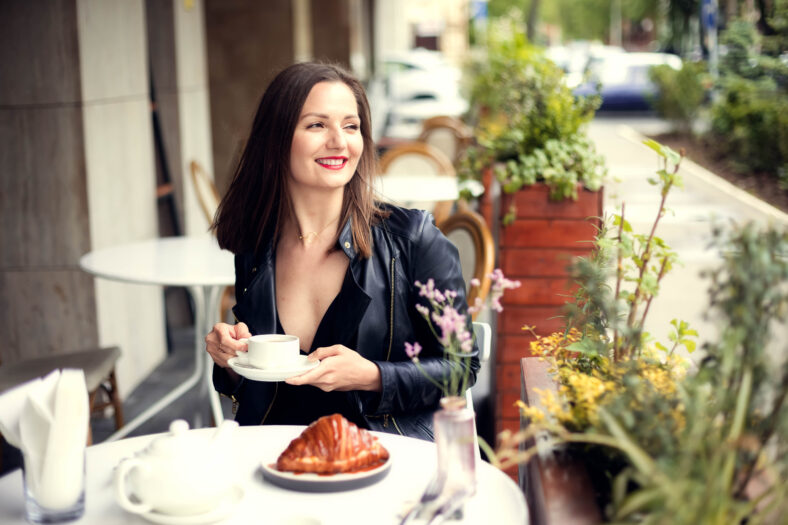 Young smiling woman in casual clothes drinking coffee in street cafe