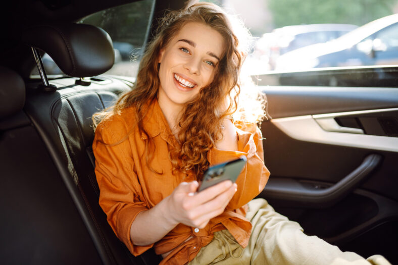 Young woman uses a smartphone while sitting in the back seat of a car. Concept of technology, traveling by car, business.