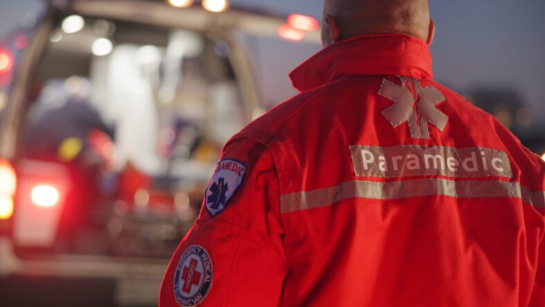 Back, man and paramedic walking to ambulance for emergency, ems service and healthcare in city. Rear view, medical professional and doctor outdoor at night for first aid, rescue operation and work.