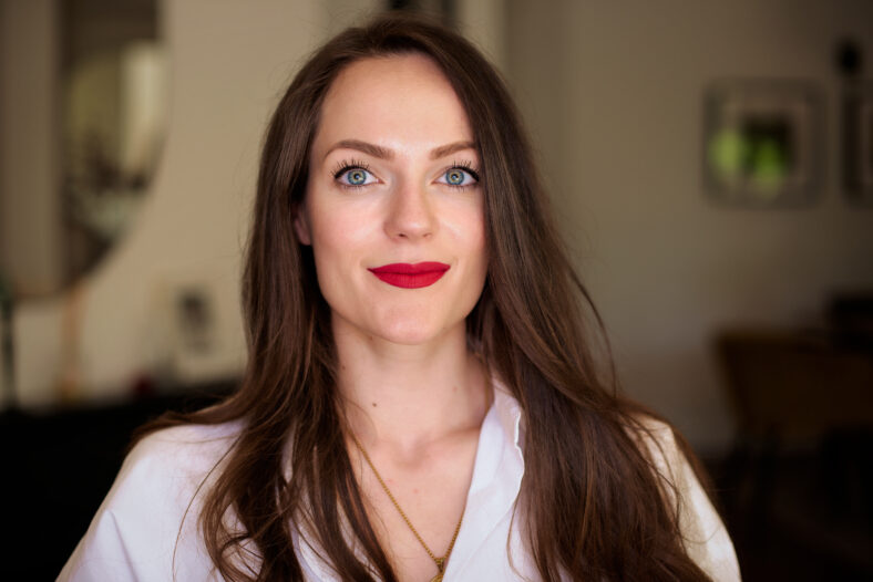 Close-up portrait of smiling young woman with green eyes. Brunette haired female wearing red lipstick and white shirt.