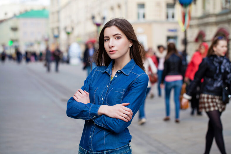 Close up Portrait of a beautiful young woman in a blue jeans shirt on the background of spring street