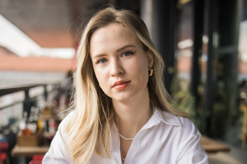 Portrait of beautiful young blonde woman drinking a cup of tea in balcony cafeteria. Happy smiling female relaxing in a coffee shop