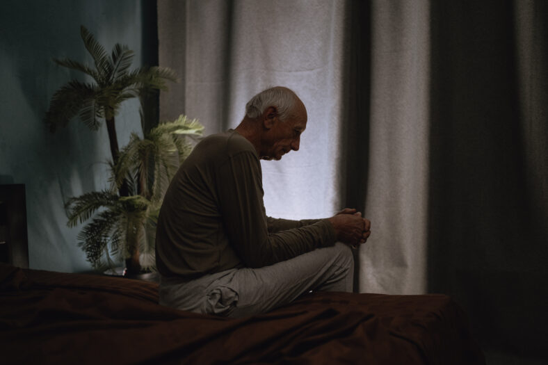 Silhouette depressed senior man 70s sits thoughtful looking down, melancholic male at night on the bed. Copy space