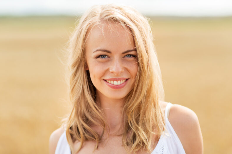 country, nature, summer holidays, vacation and people concept - smiling young woman in white on cereal field