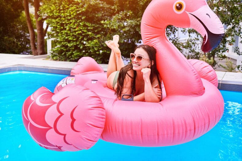 Happy girl, relax and pool with flamingo for floating, swim or summer time at holiday resort. Female person, smile or lying on pink floaty in water for aqua party, relaxation or outdoor vacation.