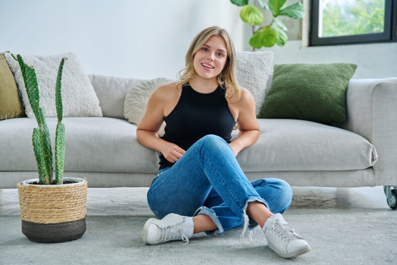 Portrait of relaxed beautiful young woman sitting at home on floor. Smiling attractive female looking at camera in living room. Leisure happiness cozy lifestyle youth concept