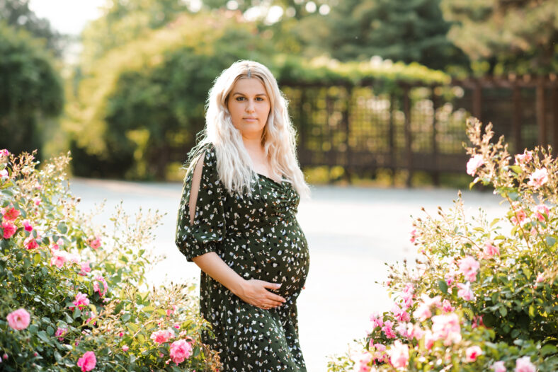Stylish pregnant woman 30-35 year old wearing dress in floral meadow with flowers outdoors. Motherhood. Springtime season.